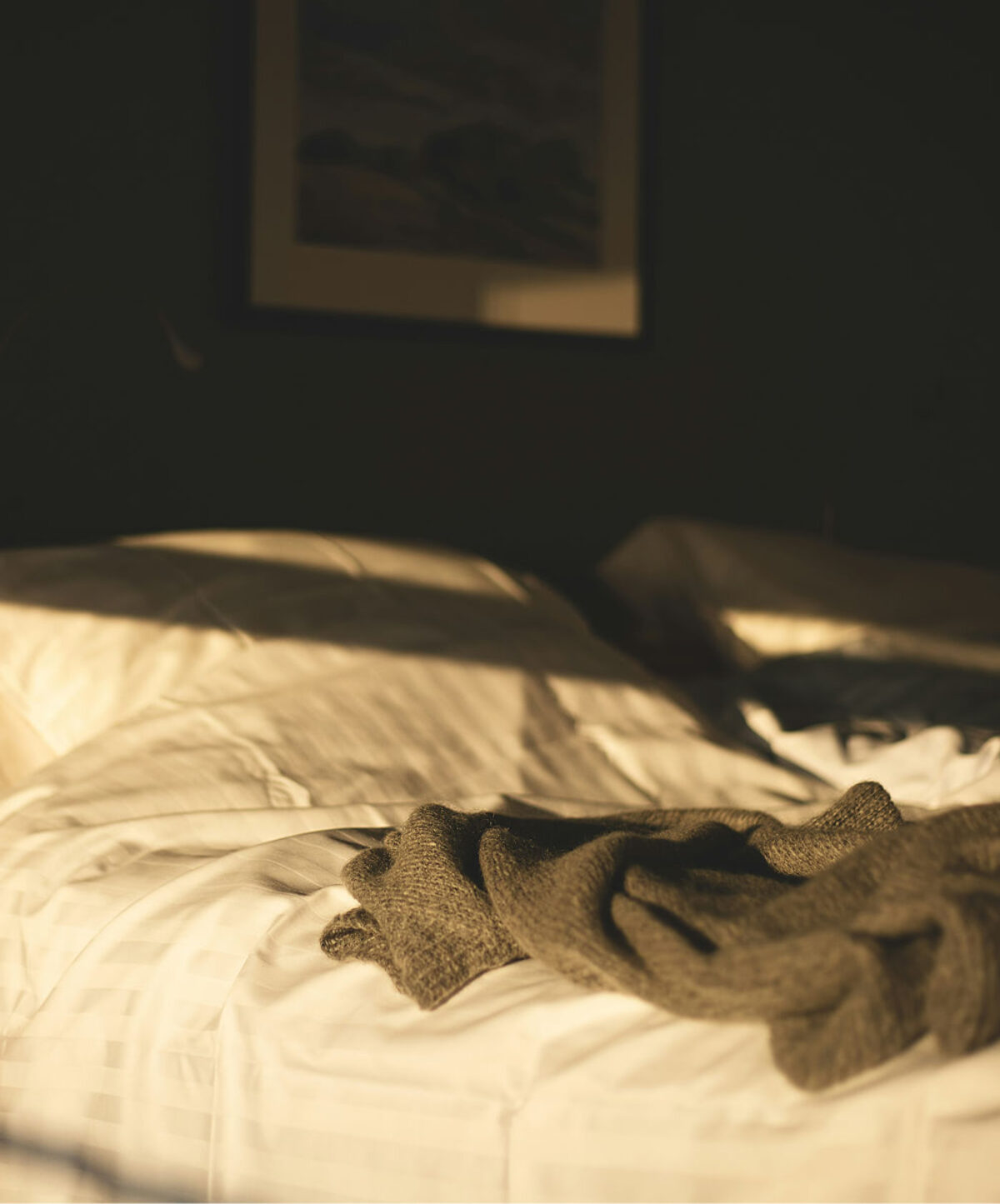 Knit blanket draped over sunlit bed linen