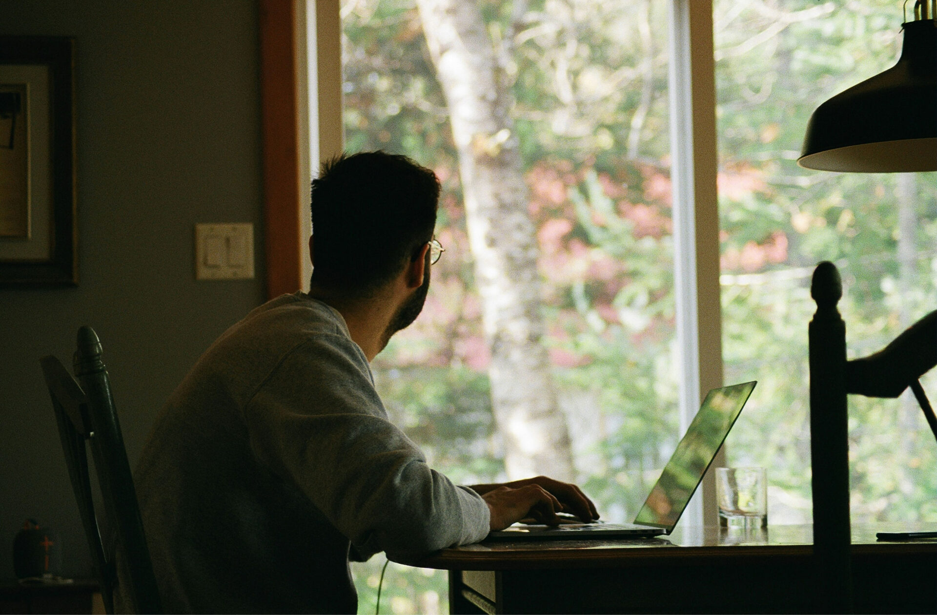 Man working on a laptop at a desk by a window with natural light