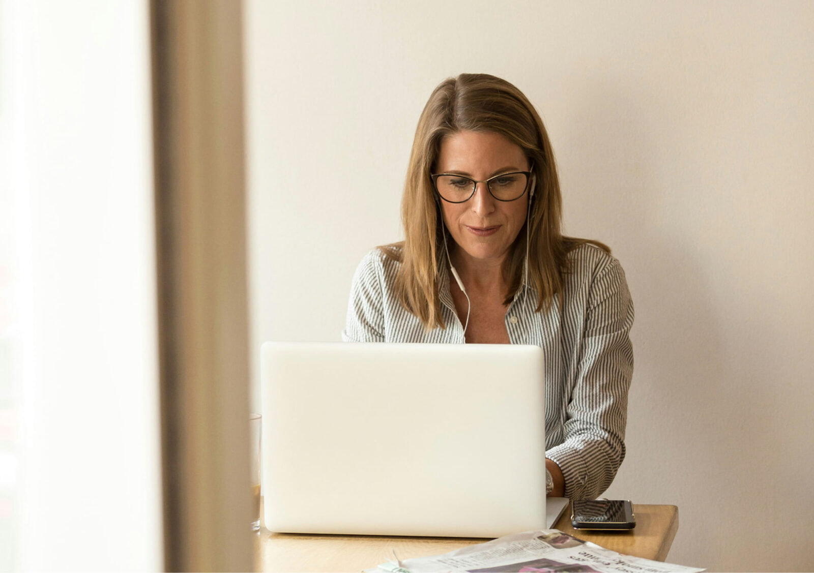 Woman wearing glasses focused on her laptop at a desk