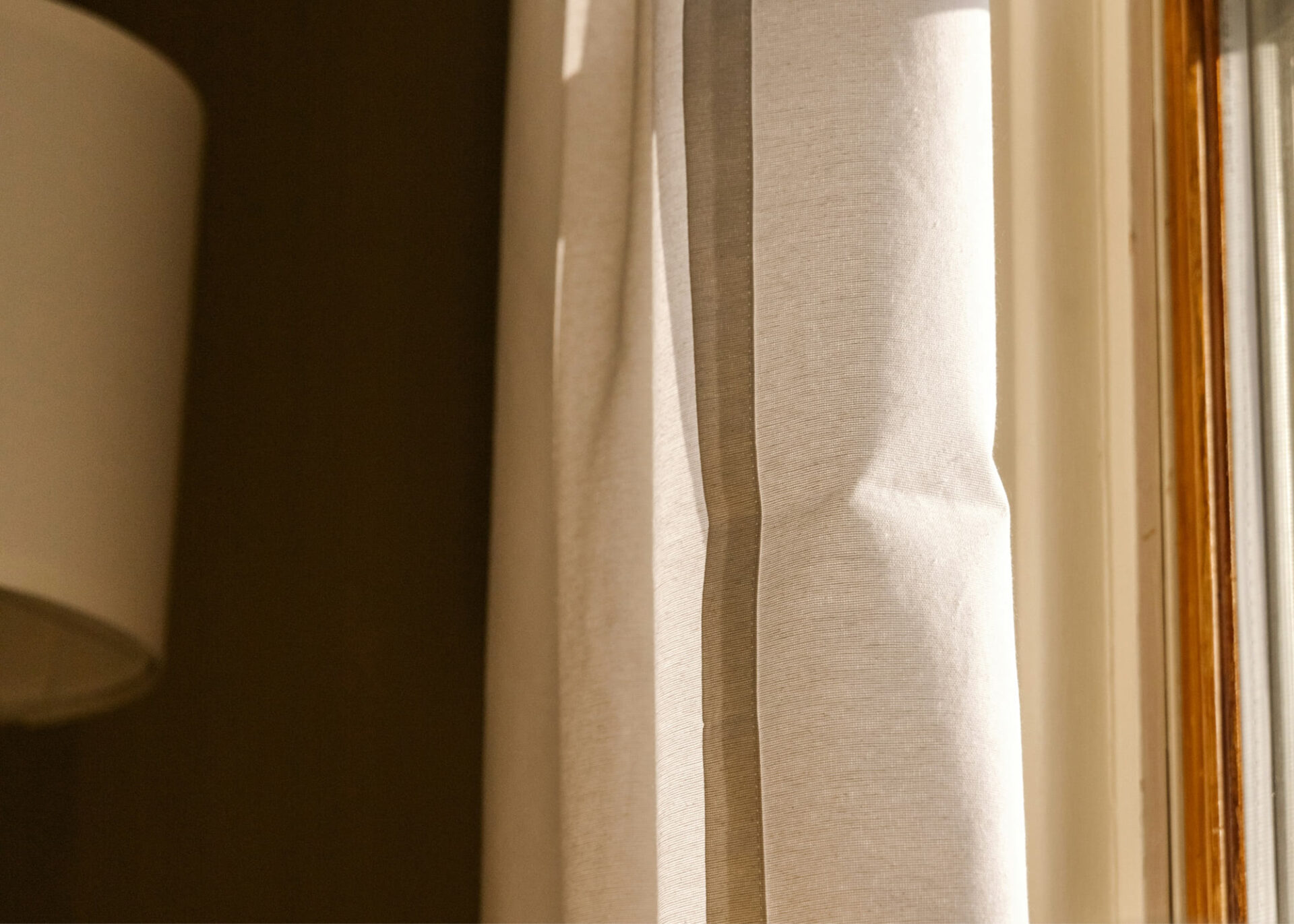Soft light falling on linen curtains beside a lamp